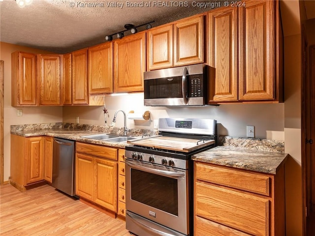 kitchen featuring sink, stainless steel appliances, light hardwood / wood-style flooring, dark stone countertops, and a textured ceiling