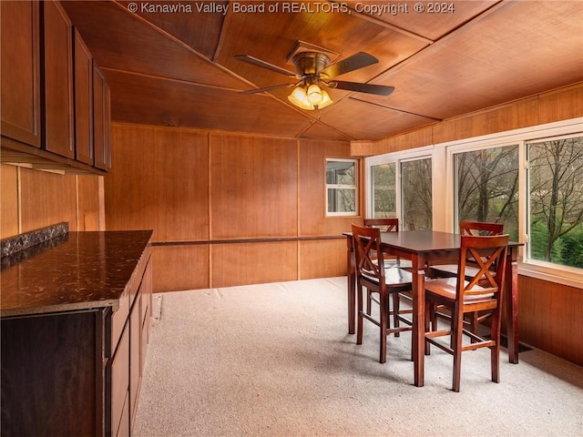 dining space featuring light colored carpet, ceiling fan, wood walls, and wood ceiling