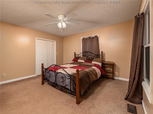 bedroom with a textured ceiling, ceiling fan, light carpet, and a closet