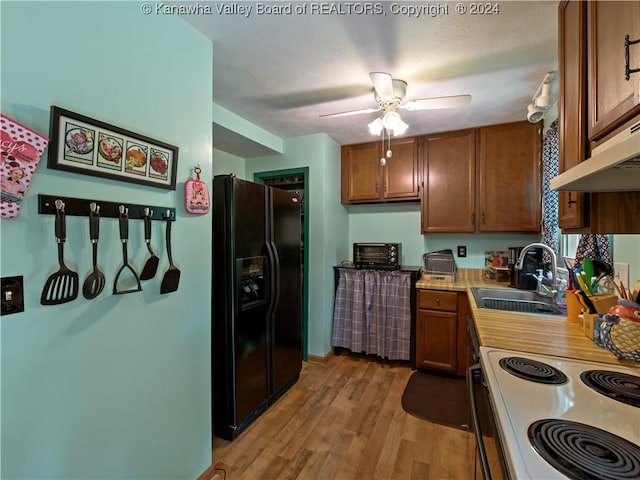 kitchen with light wood-type flooring, black fridge with ice dispenser, ventilation hood, ceiling fan, and sink