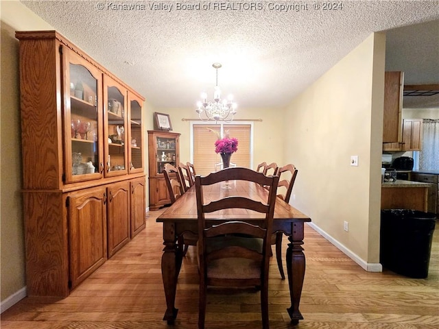 dining space with a textured ceiling, light hardwood / wood-style flooring, and an inviting chandelier