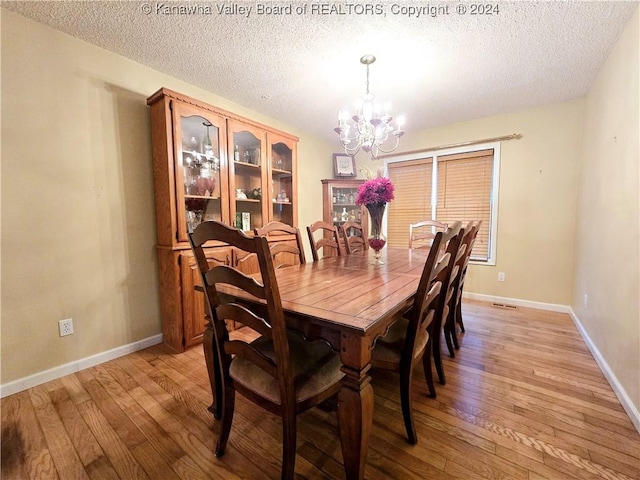 dining room featuring light wood-type flooring, a textured ceiling, and an inviting chandelier