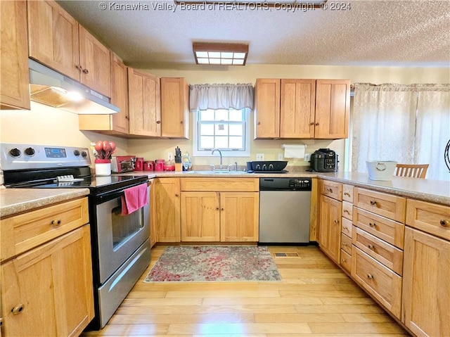 kitchen with appliances with stainless steel finishes, a textured ceiling, sink, light brown cabinets, and light hardwood / wood-style flooring