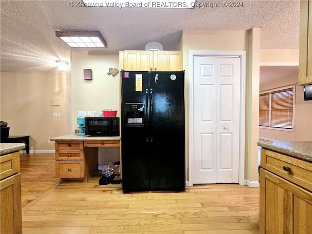 kitchen with black appliances, light brown cabinets, light wood-type flooring, and a textured ceiling