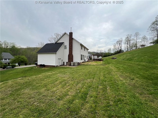 view of side of property with cooling unit, a lawn, and a chimney