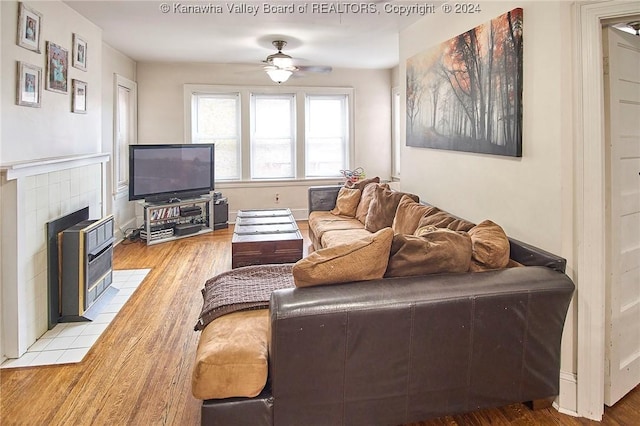 living area featuring a tile fireplace, a ceiling fan, and light wood finished floors