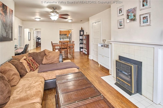 living room with heating unit, light wood-style floors, a ceiling fan, and a tiled fireplace