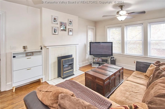 living area featuring a fireplace, baseboards, light wood finished floors, and ceiling fan