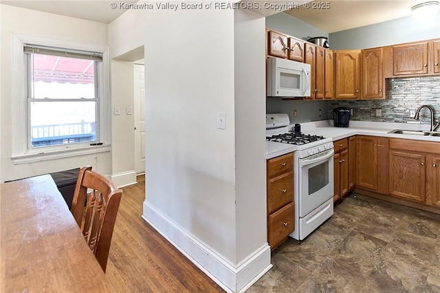 kitchen featuring white appliances, brown cabinetry, a sink, decorative backsplash, and light countertops