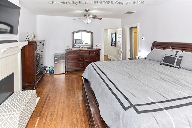 bedroom with visible vents, a fireplace, dark wood-style floors, and a ceiling fan