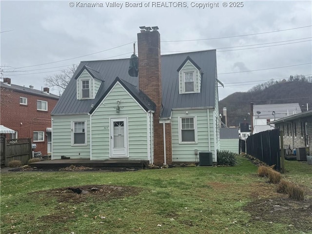 rear view of property with metal roof, a yard, a chimney, and fence