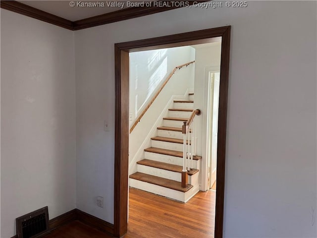 stairs with ornamental molding, visible vents, baseboards, and wood finished floors