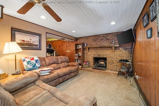 living room with wood walls, ceiling fan, light carpet, and a brick fireplace