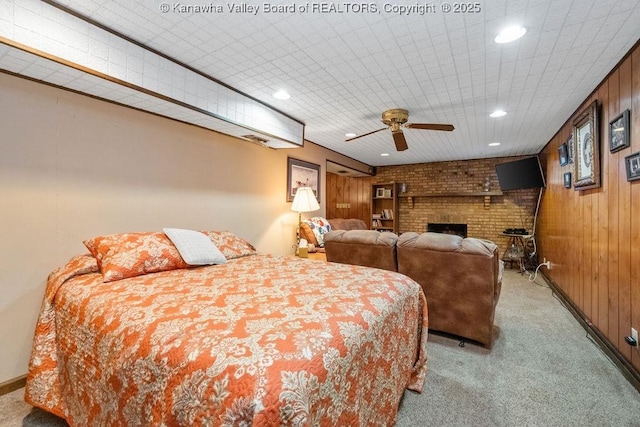 bedroom with wood walls, ceiling fan, light colored carpet, and a brick fireplace