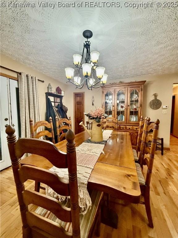 dining area with light hardwood / wood-style floors, a textured ceiling, and an inviting chandelier