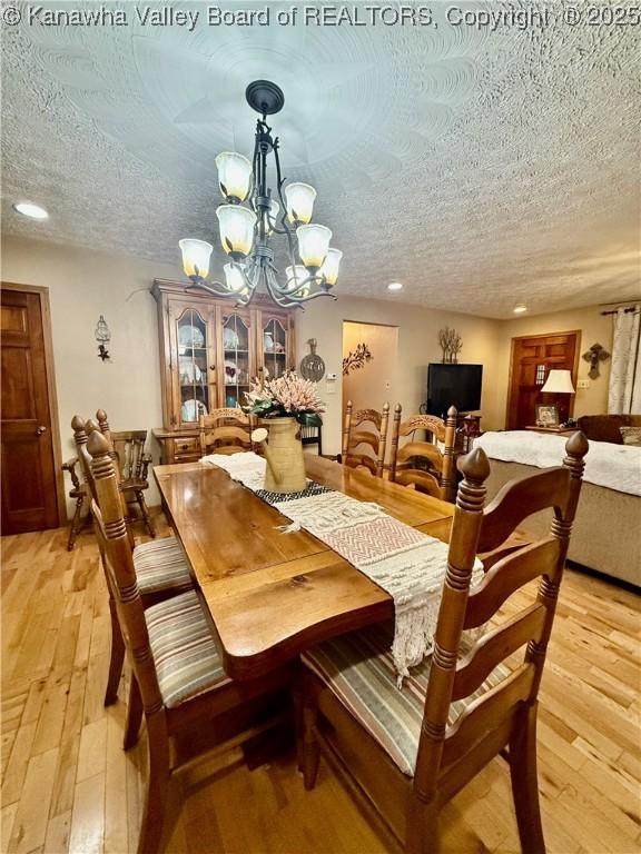 dining space with a textured ceiling, light hardwood / wood-style floors, and an inviting chandelier