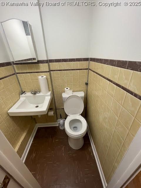 bathroom with toilet, tile walls, and sink