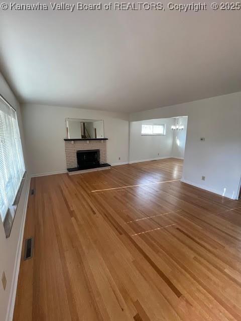 unfurnished living room with wood-type flooring, an inviting chandelier, and a brick fireplace