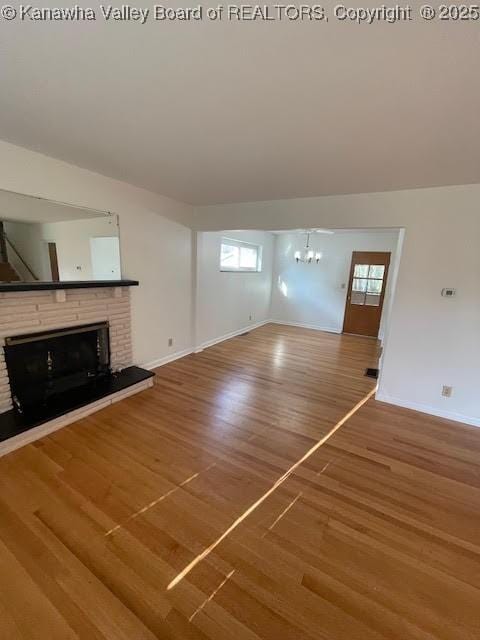 unfurnished living room featuring a fireplace, a notable chandelier, and hardwood / wood-style flooring