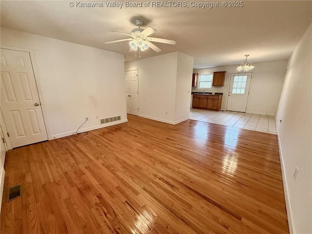 unfurnished living room with light hardwood / wood-style flooring and ceiling fan with notable chandelier