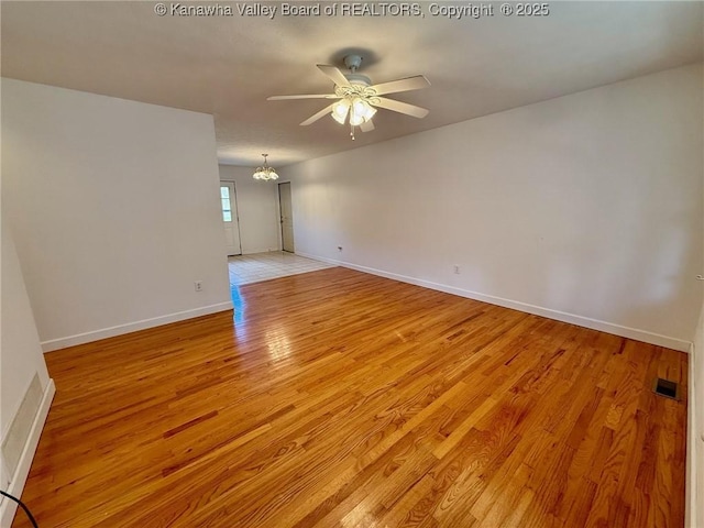 spare room featuring ceiling fan with notable chandelier and light hardwood / wood-style flooring