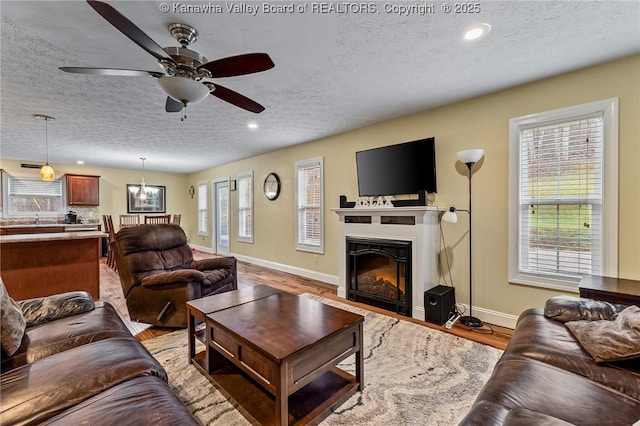 living room featuring ceiling fan with notable chandelier, a textured ceiling, and light hardwood / wood-style flooring