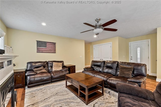 living room with ceiling fan, a textured ceiling, and light hardwood / wood-style flooring