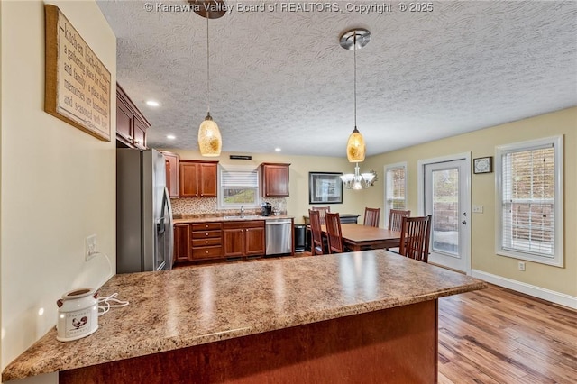 kitchen featuring decorative backsplash, a textured ceiling, appliances with stainless steel finishes, decorative light fixtures, and light hardwood / wood-style floors