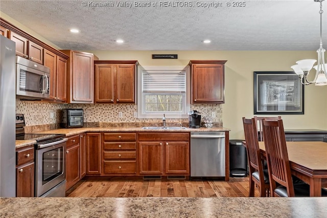 kitchen with a textured ceiling, stainless steel appliances, sink, pendant lighting, and an inviting chandelier