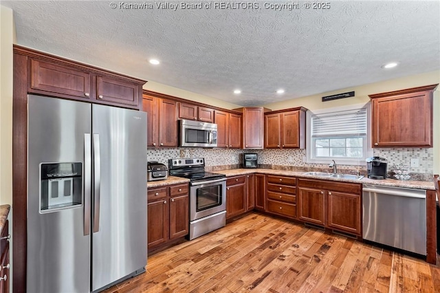 kitchen with decorative backsplash, appliances with stainless steel finishes, light wood-type flooring, a textured ceiling, and sink