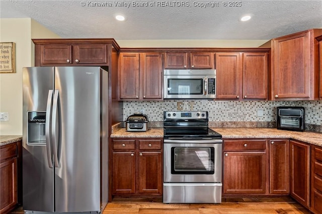 kitchen featuring decorative backsplash, light hardwood / wood-style floors, light stone counters, and appliances with stainless steel finishes