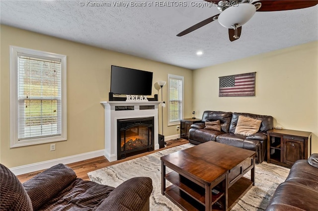 living room featuring ceiling fan, light hardwood / wood-style floors, plenty of natural light, and a textured ceiling