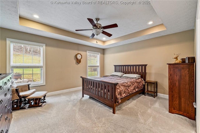 bedroom featuring light carpet, a textured ceiling, a tray ceiling, and ceiling fan