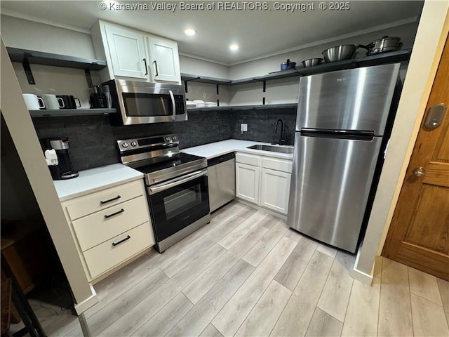 kitchen featuring backsplash, sink, light wood-type flooring, appliances with stainless steel finishes, and white cabinetry