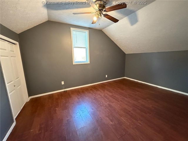 additional living space with a textured ceiling, ceiling fan, dark wood-type flooring, and vaulted ceiling