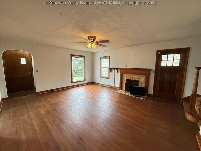 unfurnished living room featuring ceiling fan, wood-type flooring, a tiled fireplace, and a textured ceiling