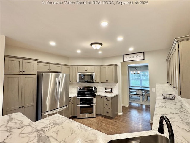 kitchen with gray cabinetry, light stone countertops, sink, stainless steel appliances, and backsplash