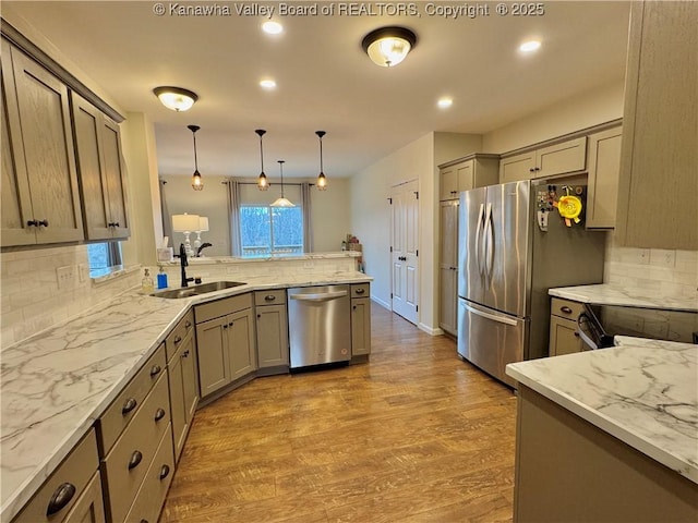 kitchen with appliances with stainless steel finishes, light wood-type flooring, light stone counters, sink, and hanging light fixtures