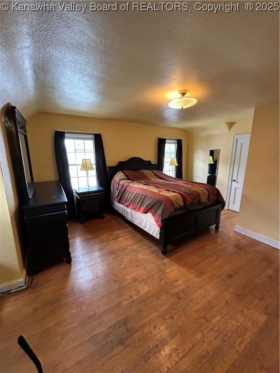 bedroom with hardwood / wood-style flooring, a textured ceiling, and vaulted ceiling