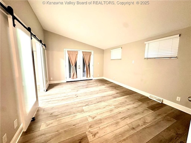 empty room with a barn door, french doors, vaulted ceiling, and light wood-type flooring