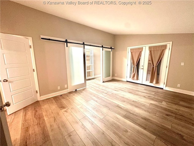 unfurnished room featuring light wood-type flooring, a barn door, and lofted ceiling