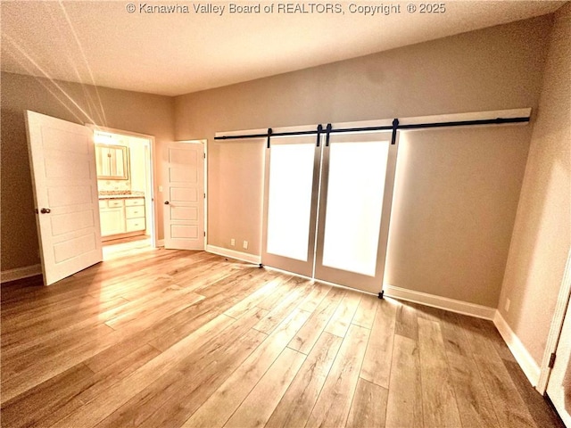 unfurnished bedroom with light wood-type flooring, a barn door, and connected bathroom