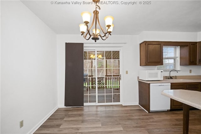 kitchen featuring white appliances, sink, wood-type flooring, pendant lighting, and an inviting chandelier