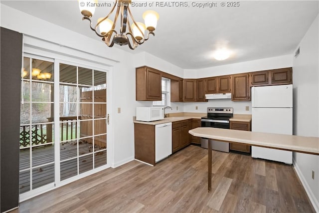 kitchen featuring white appliances, an inviting chandelier, sink, hanging light fixtures, and wood-type flooring