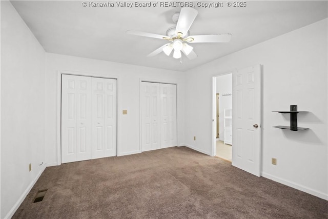 unfurnished bedroom featuring dark carpet, ceiling fan, and multiple closets