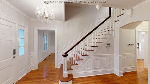 foyer entrance featuring hardwood / wood-style flooring, crown molding, and a notable chandelier