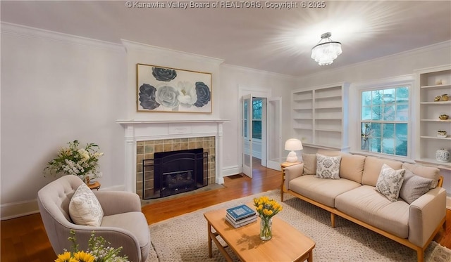 living room featuring ornamental molding, hardwood / wood-style flooring, built in features, a notable chandelier, and a tiled fireplace