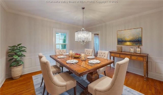 dining space with hardwood / wood-style floors, ornamental molding, and an inviting chandelier