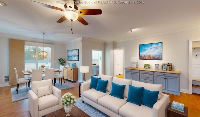 living room featuring light wood-type flooring, ceiling fan with notable chandelier, and ornamental molding