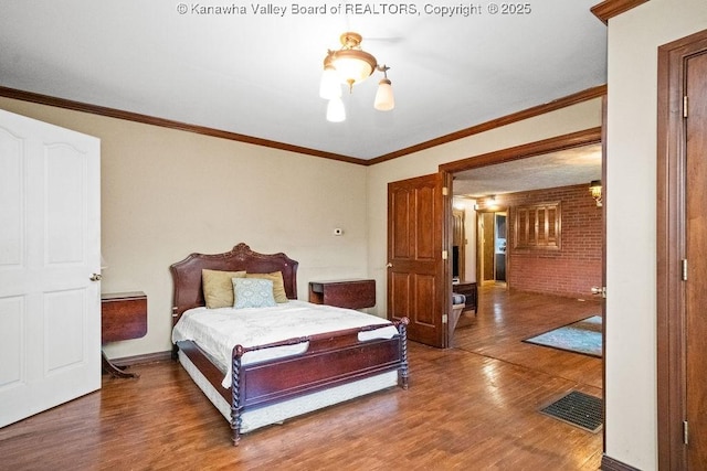 bedroom with ornamental molding, hardwood / wood-style flooring, a notable chandelier, and brick wall